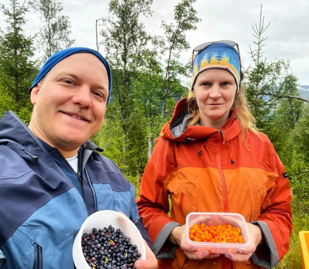 Two people showing bowls of freshly picked blueberries and cloudberries