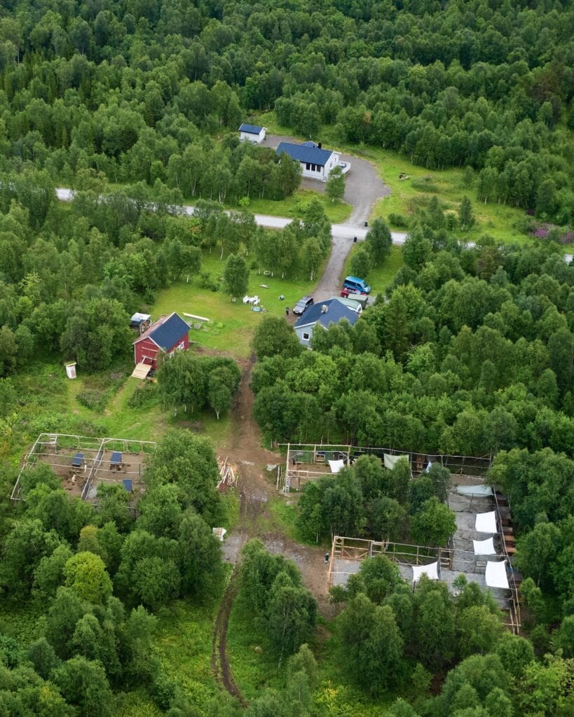 Aerial view of the husky farm with red house, dog enclosures, and birch forest