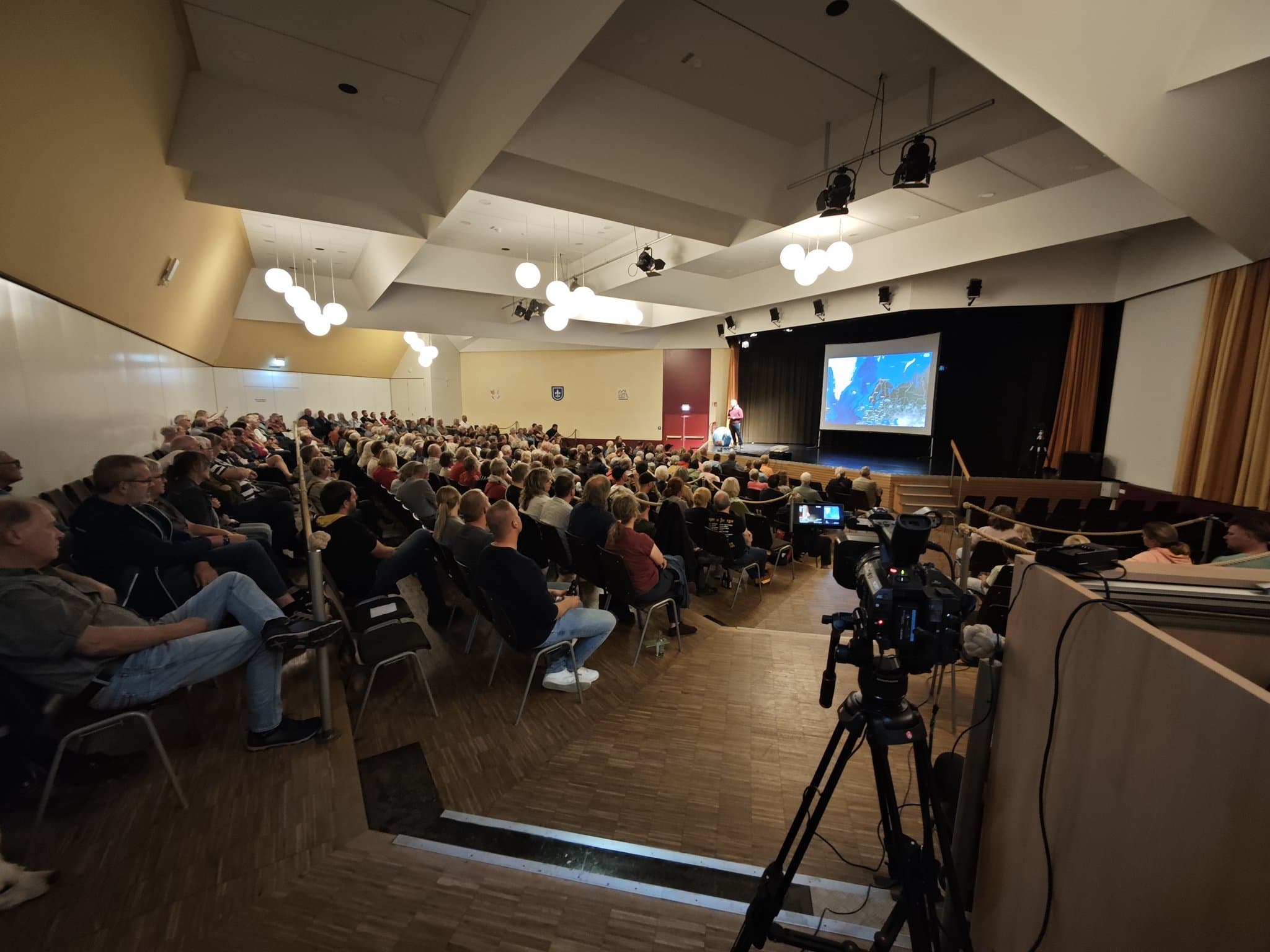 Voll besetzter Saal im Pädagogischen Zentrum Warburg beim Vortrag „Am Rand der Welt“, vorne eine Videokamera auf dem Stativ