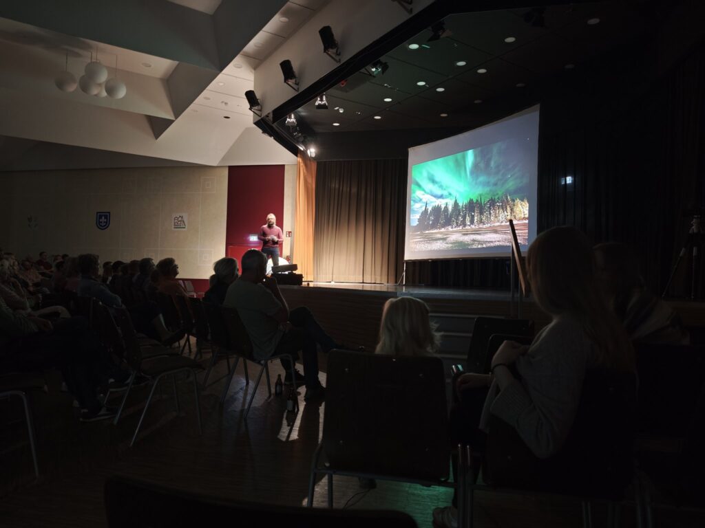 Lukas auf der Bühne, auf der Leinwand Nordlichter über einem Nadelwald